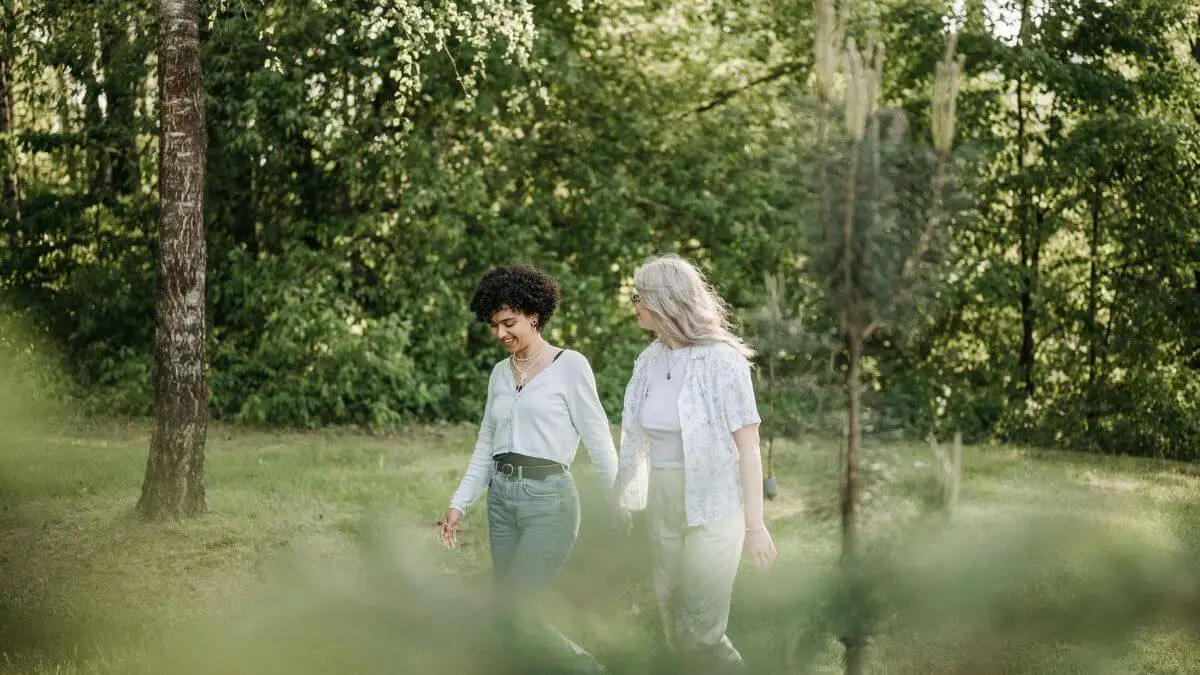 Duas mulheres caminhando juntas ao ar livre em meio à natureza, transmitindo amizade, leveza e conexão genuína.