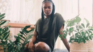 Mulher sentada em ambiente aconchegante com plantas ao redor, postura tranquila e expressão serena.