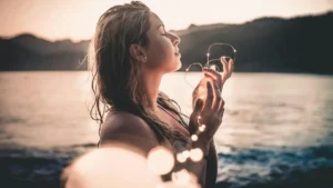 Mulher de olhos fechados com expressão serena segurando luzes ao entardecer em momento de mindfulness e presença
