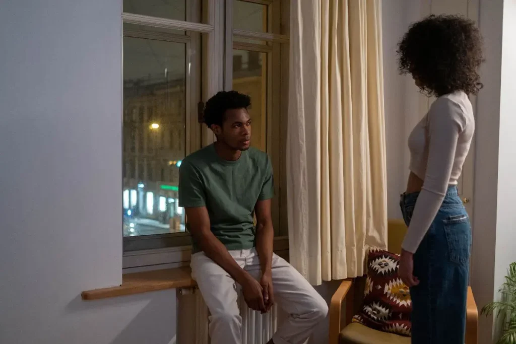 Casal em ambiente doméstico durante conversa difícil, com expressões tensas e postura distante, transmitindo conflito emocional e falta de conexão.