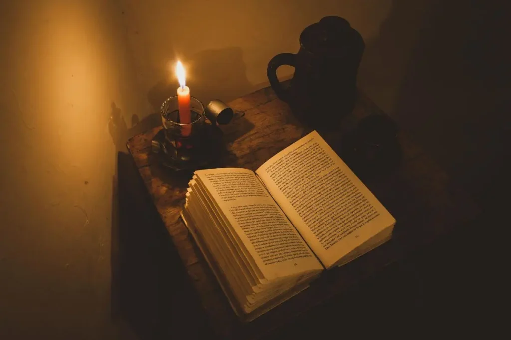 Livro aberto sobre mesa de cabeceira com vela acesa e caneca ao fundo criando ambiente noturno aconchegante para ritual de sono