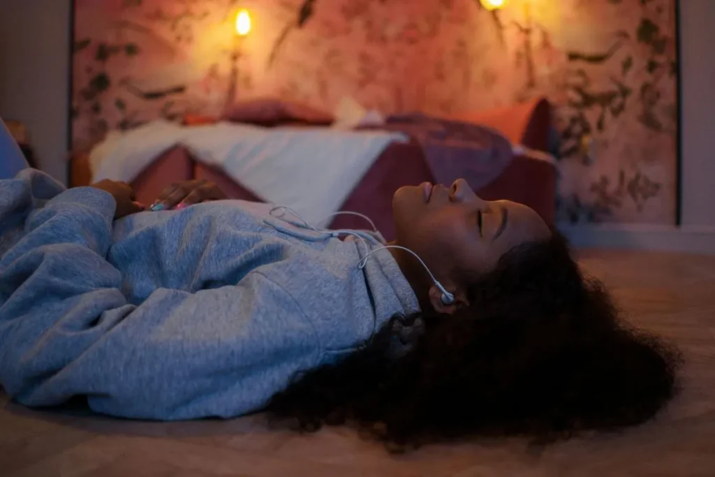 Mulher deitada em postura relaxada com olhos fechados, em ambiente acolhedor com luz quente ao fundo, transmitindo calma, presença e descanso emocional.