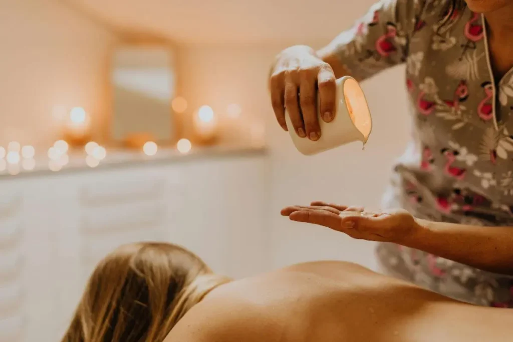 Mulher deitada em ambiente acolhedor recebendo massagem relaxante, com vela acesa e luz quente ao fundo.