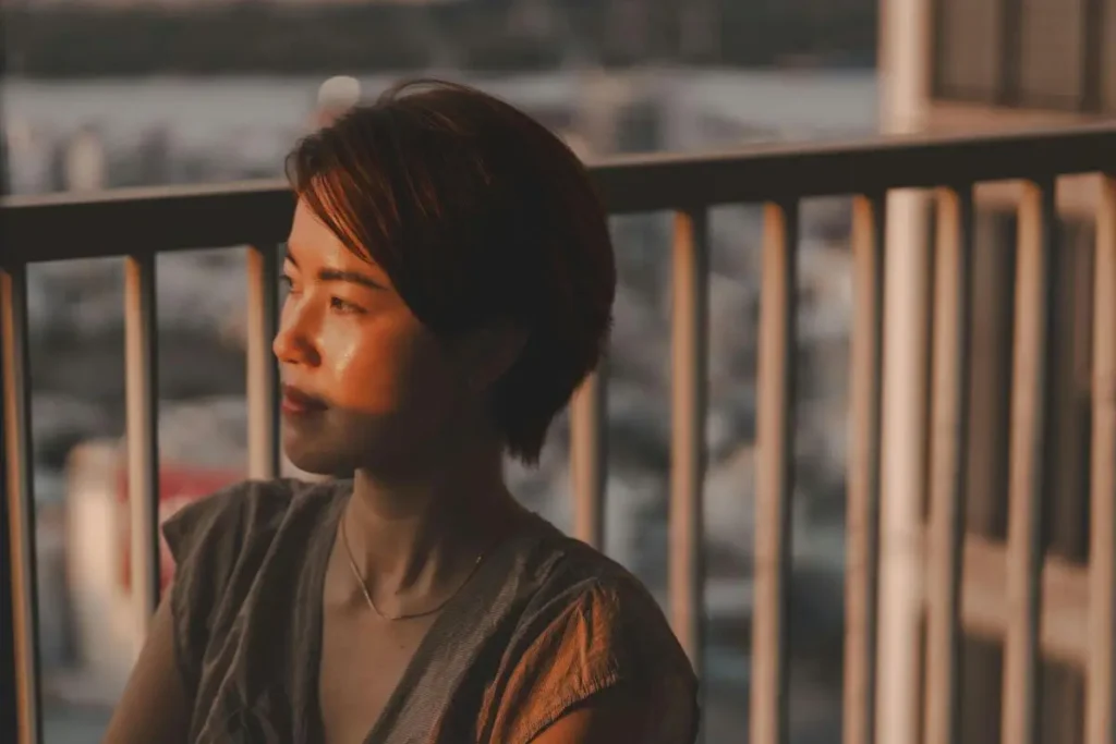 Mulher com olhar distante e expressão introspectiva à luz dourada do entardecer em varanda