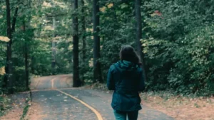 Mulher caminhando sozinha em caminho arborizado, com postura tranquila e sensação de presença em meio à natureza.