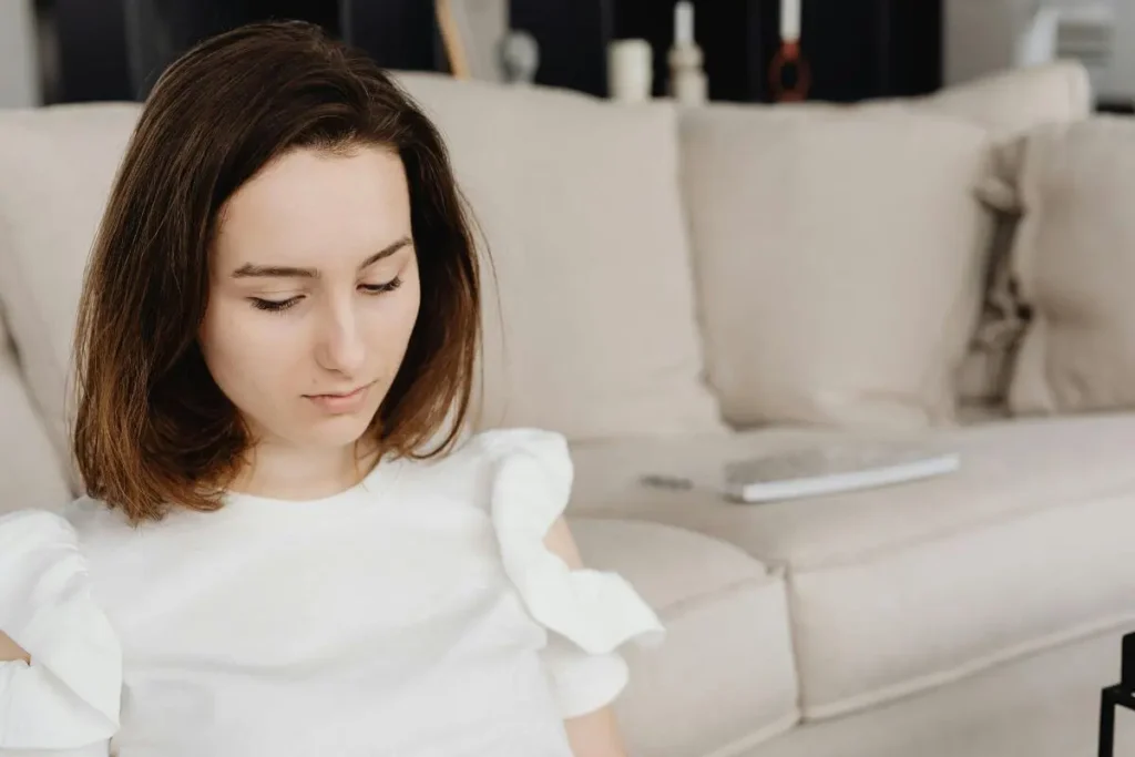 Mulher com olhar voltado para baixo e expressão pensativa em ambiente acolhedor neutro transmitindo peso interno e introspecção