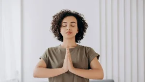 Mulher com olhos fechados e mãos juntas no peito em postura de respiração consciente e regulação emocional