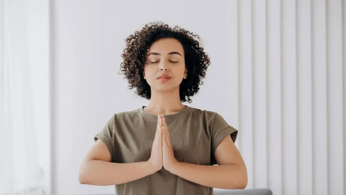 Mulher com olhos fechados e mãos juntas no peito em postura de respiração consciente e regulação emocional