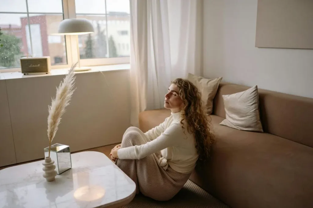 Mulher sentada no chão com olhos fechados e expressão serena em momento de pausa consciente em ambiente acolhedor com luz natural suave