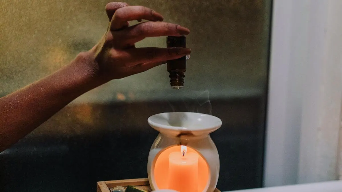 mão pingando óleo essencial em difusor aromático com vela acesa em luz quente