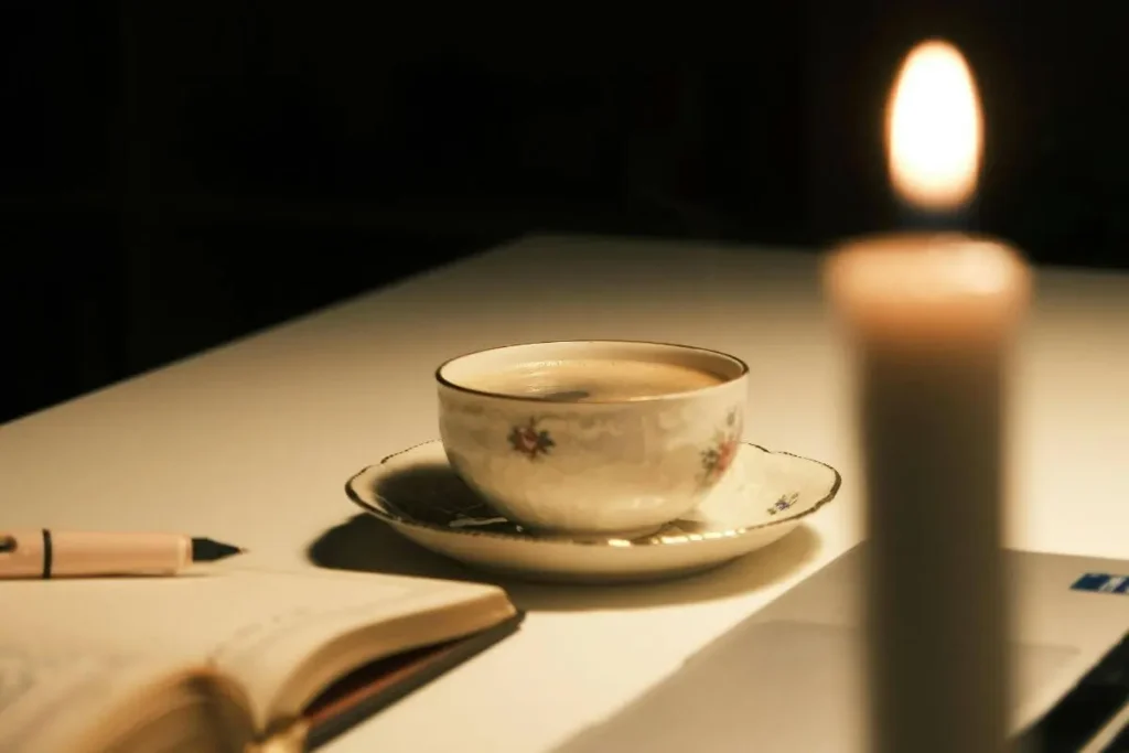 Xícara de chá sobre mesinha com caderno aberto e vela acesa ao fundo, criando uma atmosfera acolhedora de calma e pausa consciente.