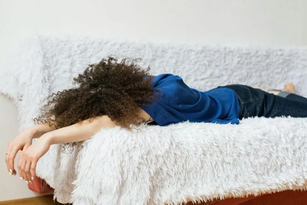 Pessoa deitada de bruços no sofá com cabelos cacheados cobrindo o rosto representando esgotamento emocional e burnout