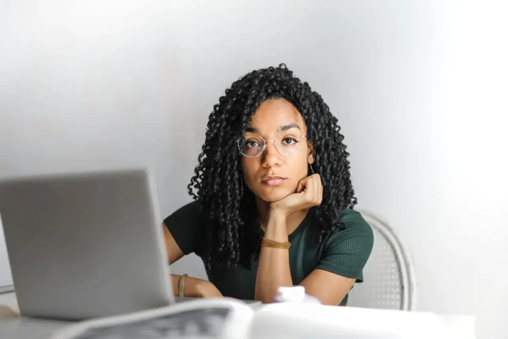 Mulher sentada em frente ao computador com expressão ausente e olhar distante, transmitindo cansaço emocional e desconexão interna.
