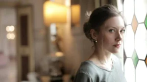 Mulher olhando para frente com expressão distante em ambiente doméstico com luz suave, transmitindo ausência emocional e introspecção.