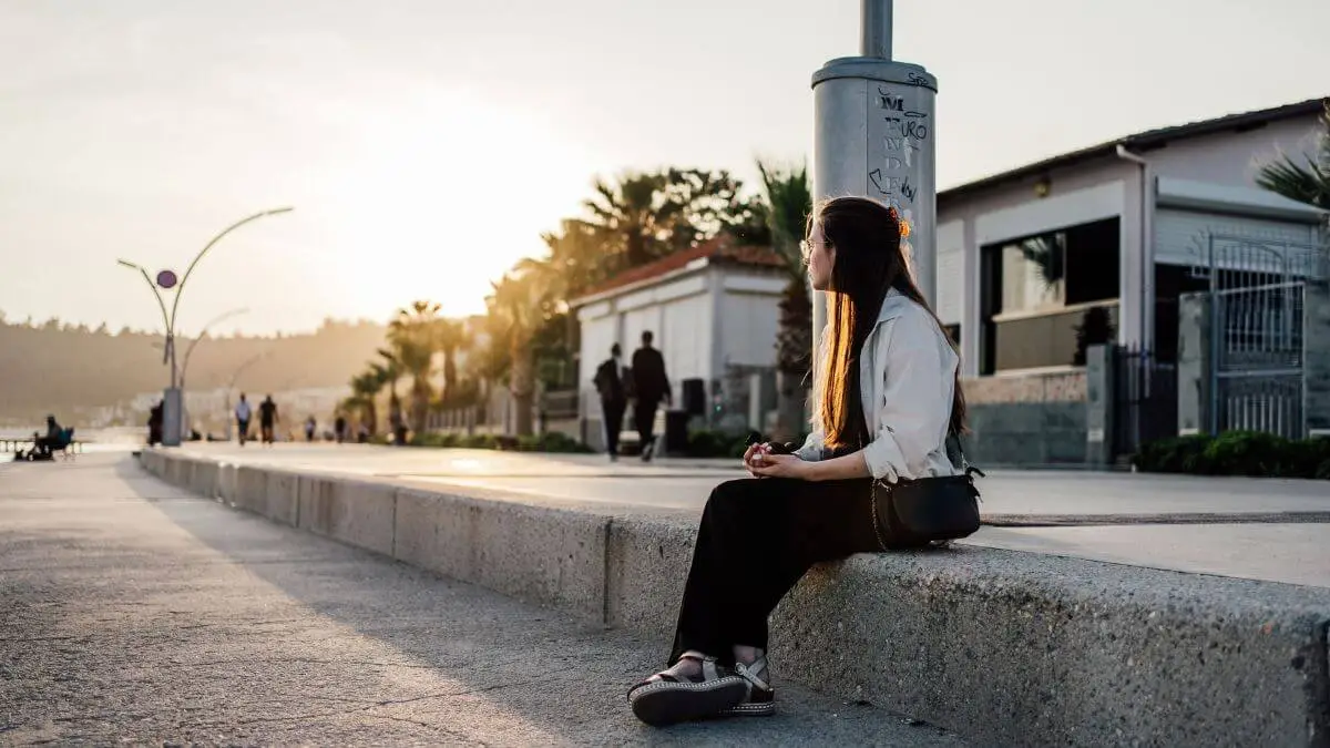 Mulher sentada sozinha ao ar livre, olhando para longe com expressão distante, transmitindo vazio emocional e introspecção.