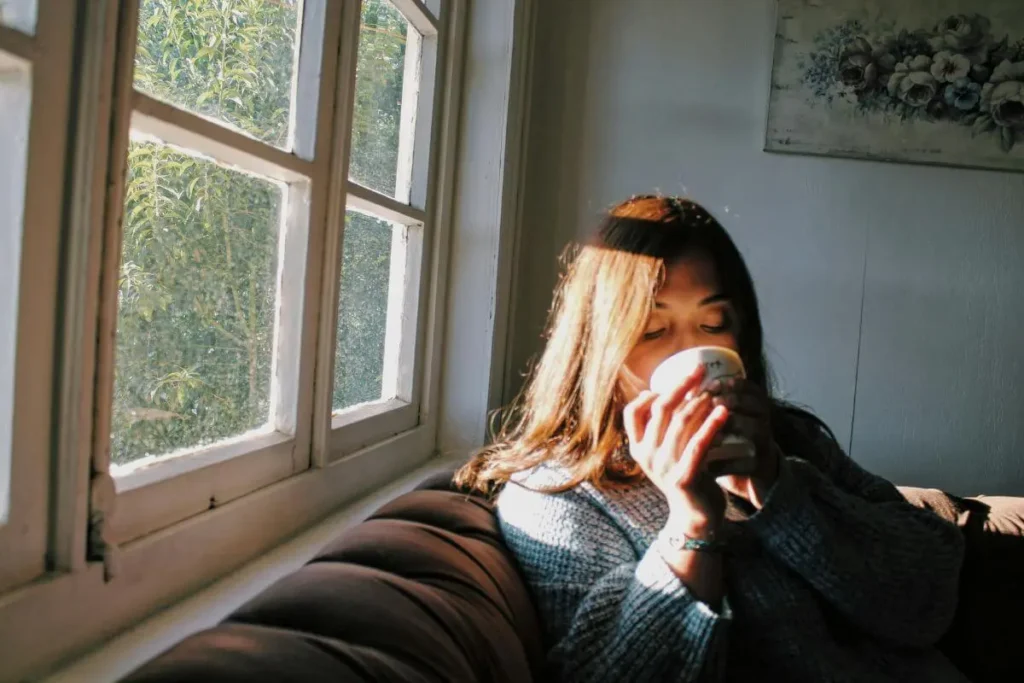 Mulher tomando chá junto à janela com luz natural dourada em momento tranquilo e acolhedor