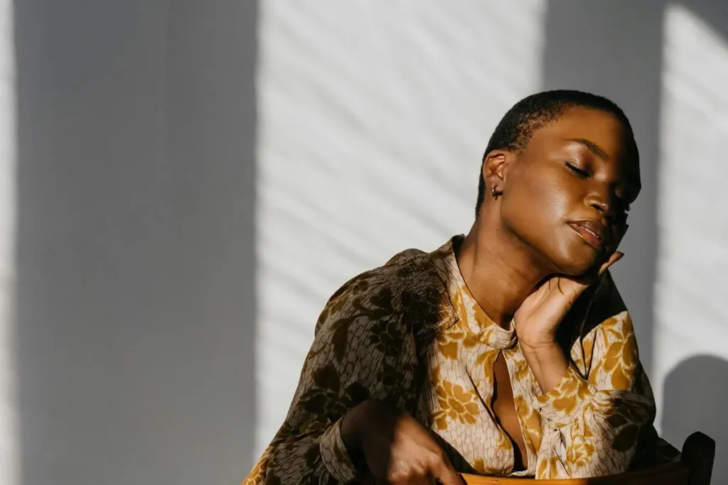 Pessoa de olhos fechados com expressão serena e luz natural suave representando momento de autocuidado e recuperação do burnout