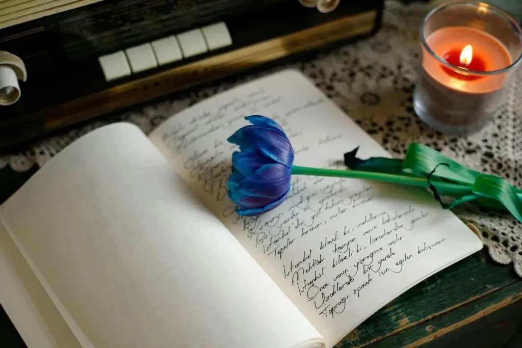 Caderno aberto com escrita à mão, flor decorativa e vela acesa ao lado, em ambiente aconchegante com luz suave.