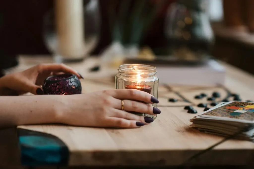 Mãos femininas próximas a uma vela acesa sobre mesa de madeira, em ambiente íntimo e acolhedor.