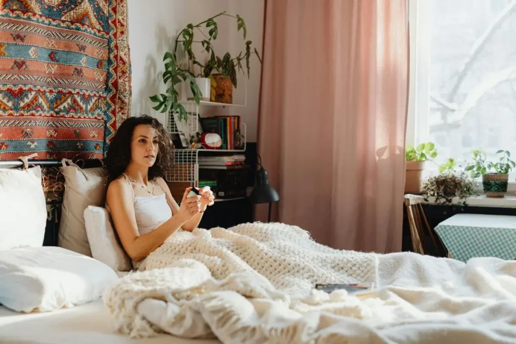 Mulher deitada na cama com olhar distante e expressão introspectiva em quarto acolhedor com luz natural suave transmitindo solidão emocional silenciosa