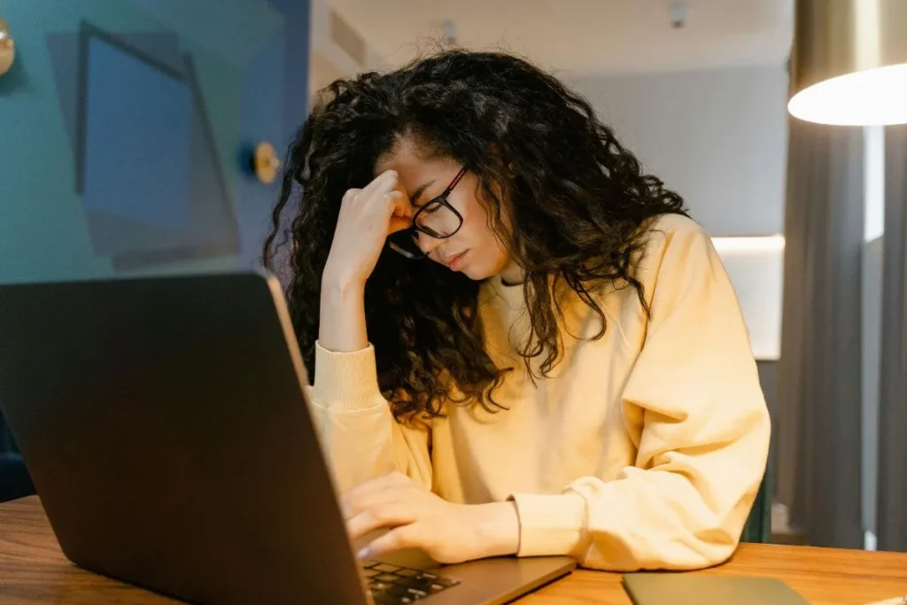 Mulher cansada com a cabeça apoiada na mão enquanto trabalha em frente ao notebook em ambiente de home office.