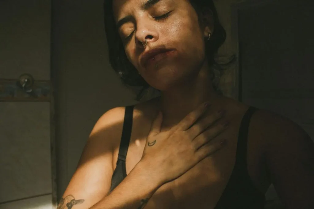 Mulher com os olhos fechados e a mão apoiada no peito, expressando tensão contida e tentativa de se acalmar.