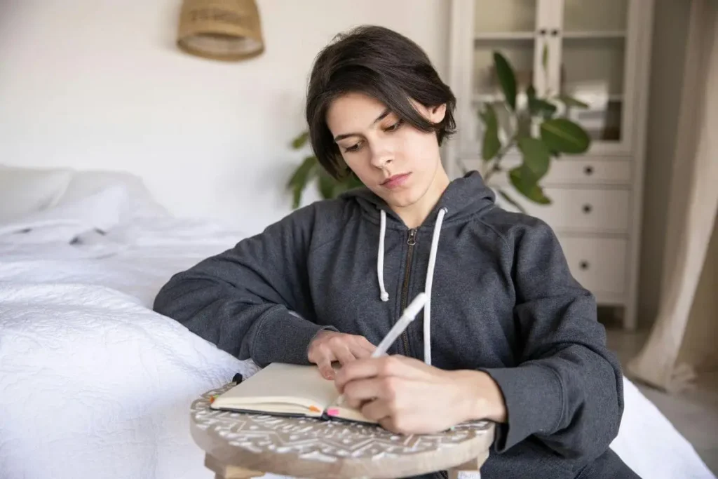 Mulher escrevendo em um caderno em ambiente acolhedor, praticando exercício de reflexão para fortalecer a resiliência emocional.