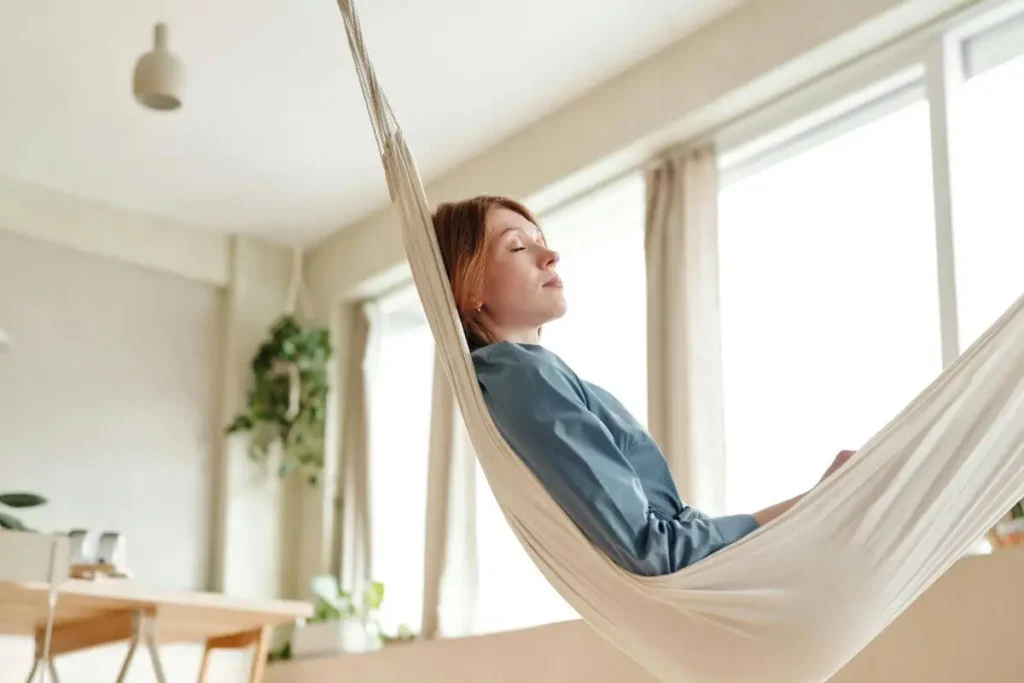 Mulher deitada em rede com olhos fechados e expressão serena em momento de pausa consciente em ambiente acolhedor com luz natural suave