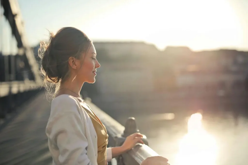 Mulher serena e determinada olhando para o horizonte sob luz natural suave, transmitindo presença e consciência.