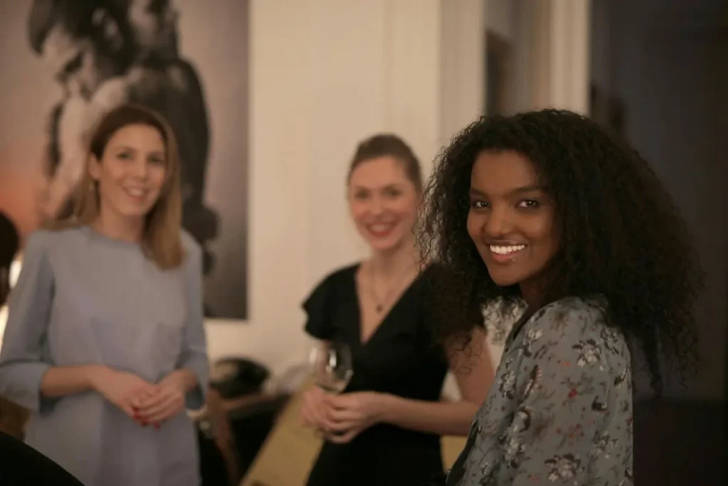 Mulher sorrindo em ambiente social com outras pessoas ao fundo, transmitindo leveza, presença e abertura emocional.