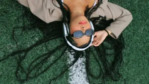 Mulher deitada na grama usando fones de ouvido, em momento de pausa, relaxamento e conexão consigo mesma.