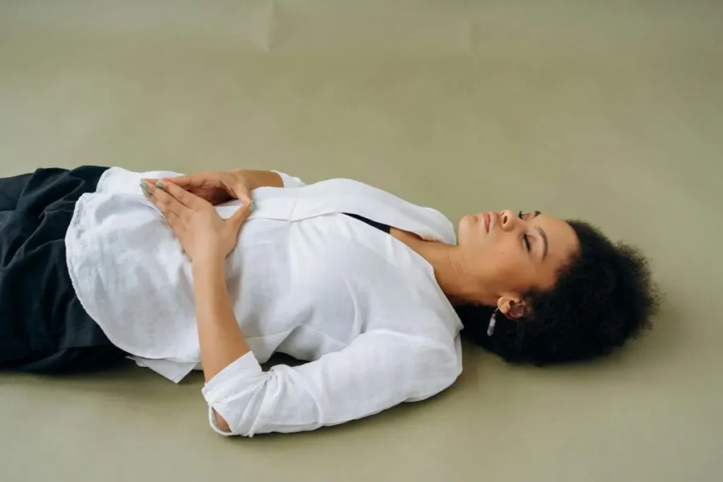 Mulher deitada com as mãos sobre o abdômen, praticando respiração diafragmática em ambiente tranquilo e minimalista.