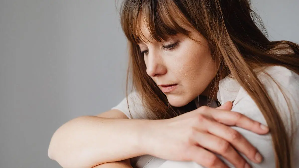 Mulher sentada com expressão triste e reflexiva, apoiada nos braços, transmitindo sensação de aperto emocional e desconforto interno.