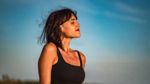 Mulher ao ar livre com os olhos fechados, respirando fundo e expressão tranquila de alívio, sob luz natural suave.