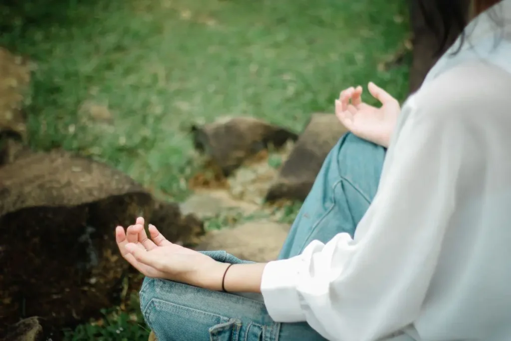 Mulher sentada em meio à natureza praticando meditação com as mãos apoiadas sobre os joelhos