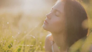 Mulher com os olhos fechados em um campo iluminado pelo sol, transmitindo serenidade e equilíbrio emocional